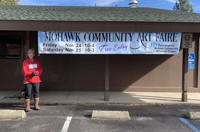 Local volunteer Nancy Degger hangs the Mohawk Community Art Faire banner at the Graeagle Fire Hall. Photo by John Lullo
